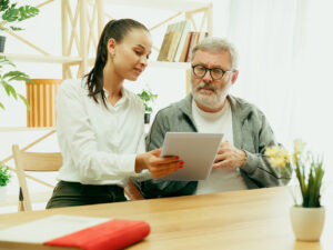 A daughter or granddaughter spends time with the grandfather or senior man. Family or fathers' day, emotions and happieness. Lifestyle portrait at home. Girl taking care about dad. Using a tablet.